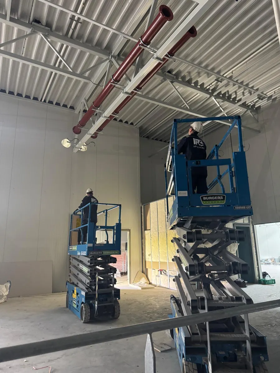 Leidinginstallatie in een bedrijfshal met hoogwerkers.